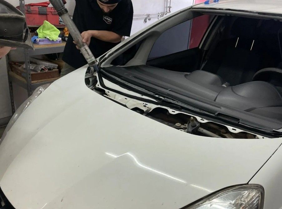 Person removing windshield from white car in a garage.