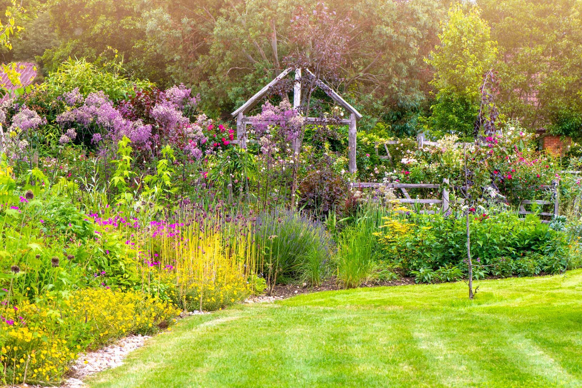 Lush garden with a grassy lawn, a small wooden structure, and diverse colorful flowers.