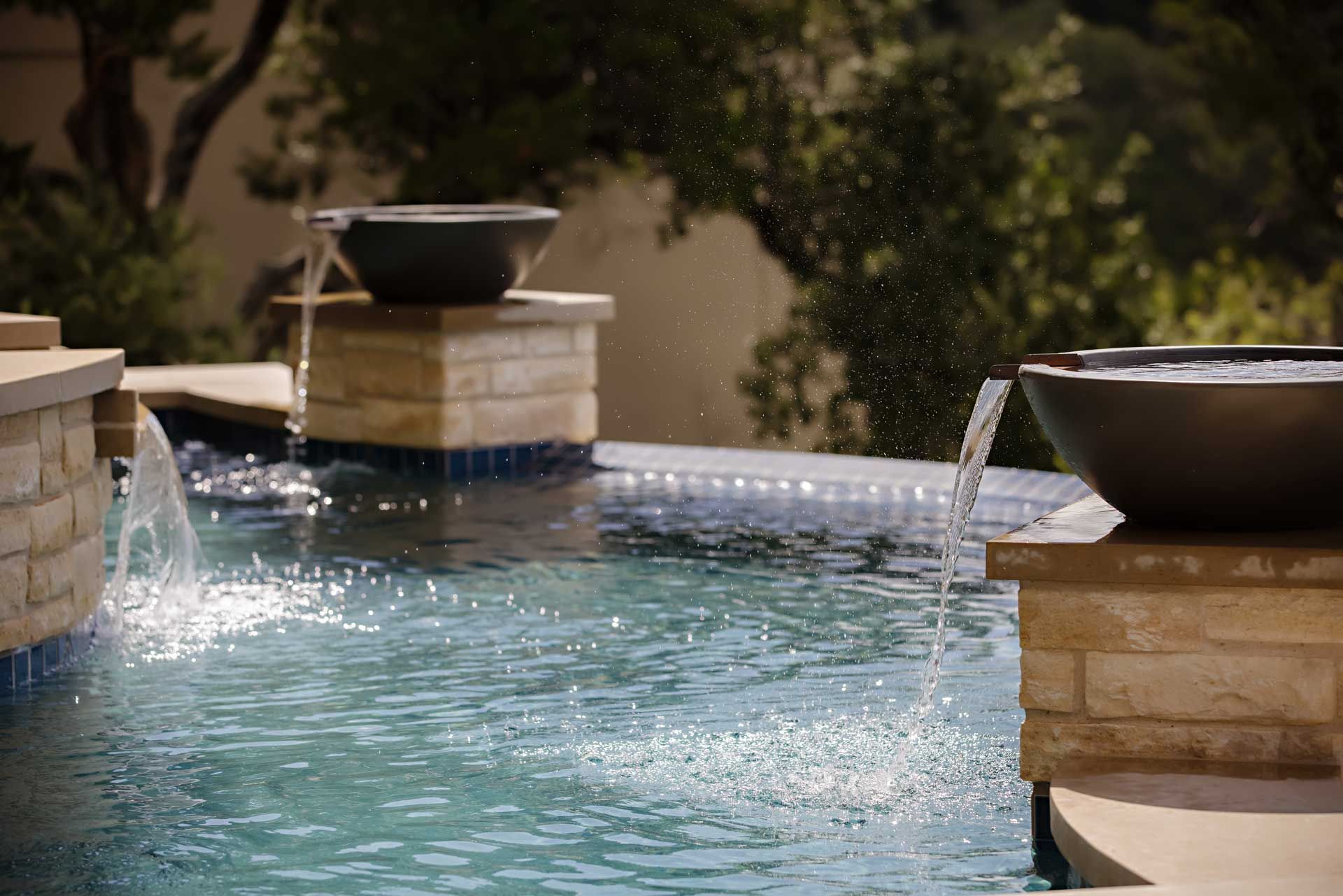 Water flows from bowls into a pool with stone features, under a sunny sky.
