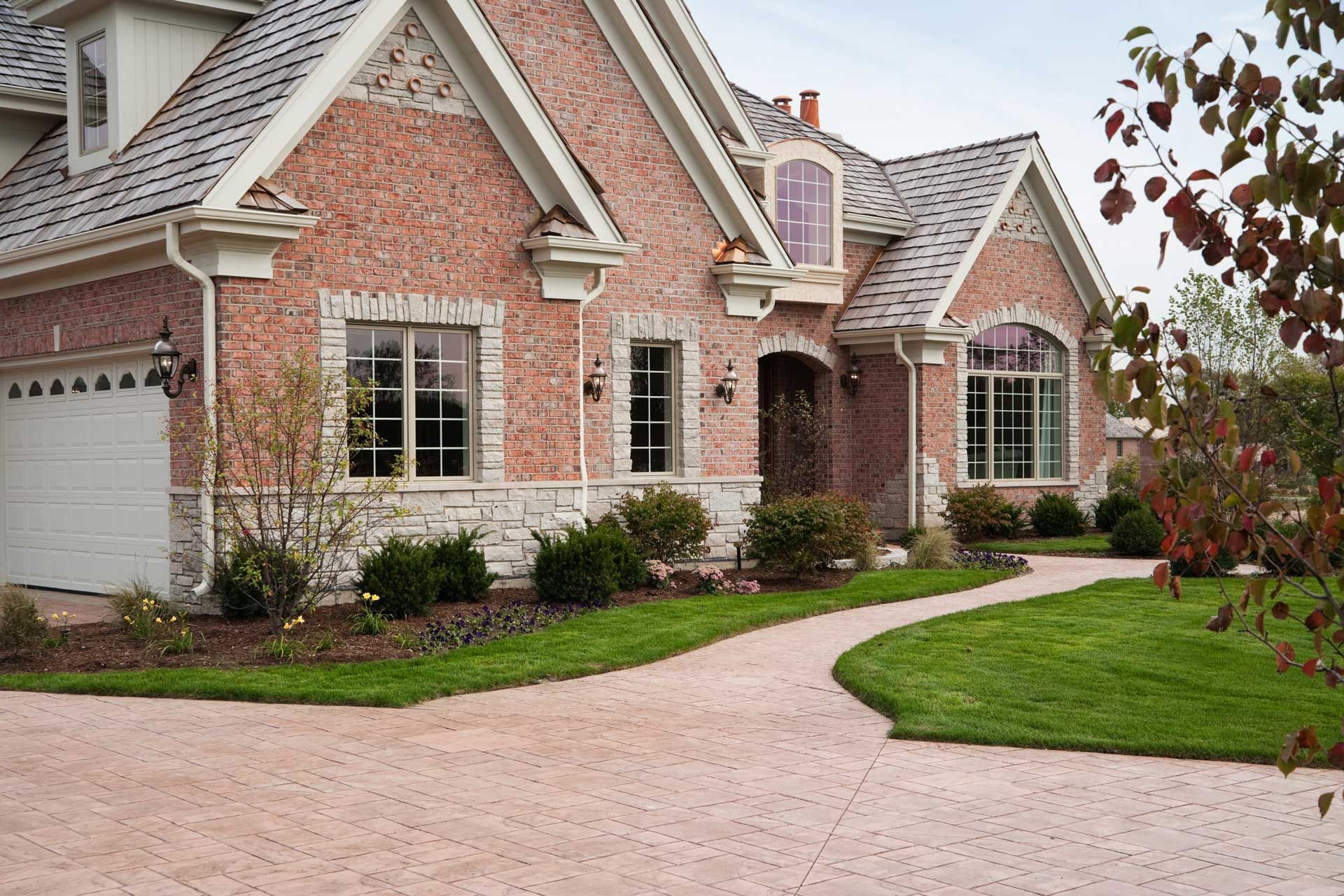 Brick house with stone accents, arched doorway, curved walkway, and manicured lawn.