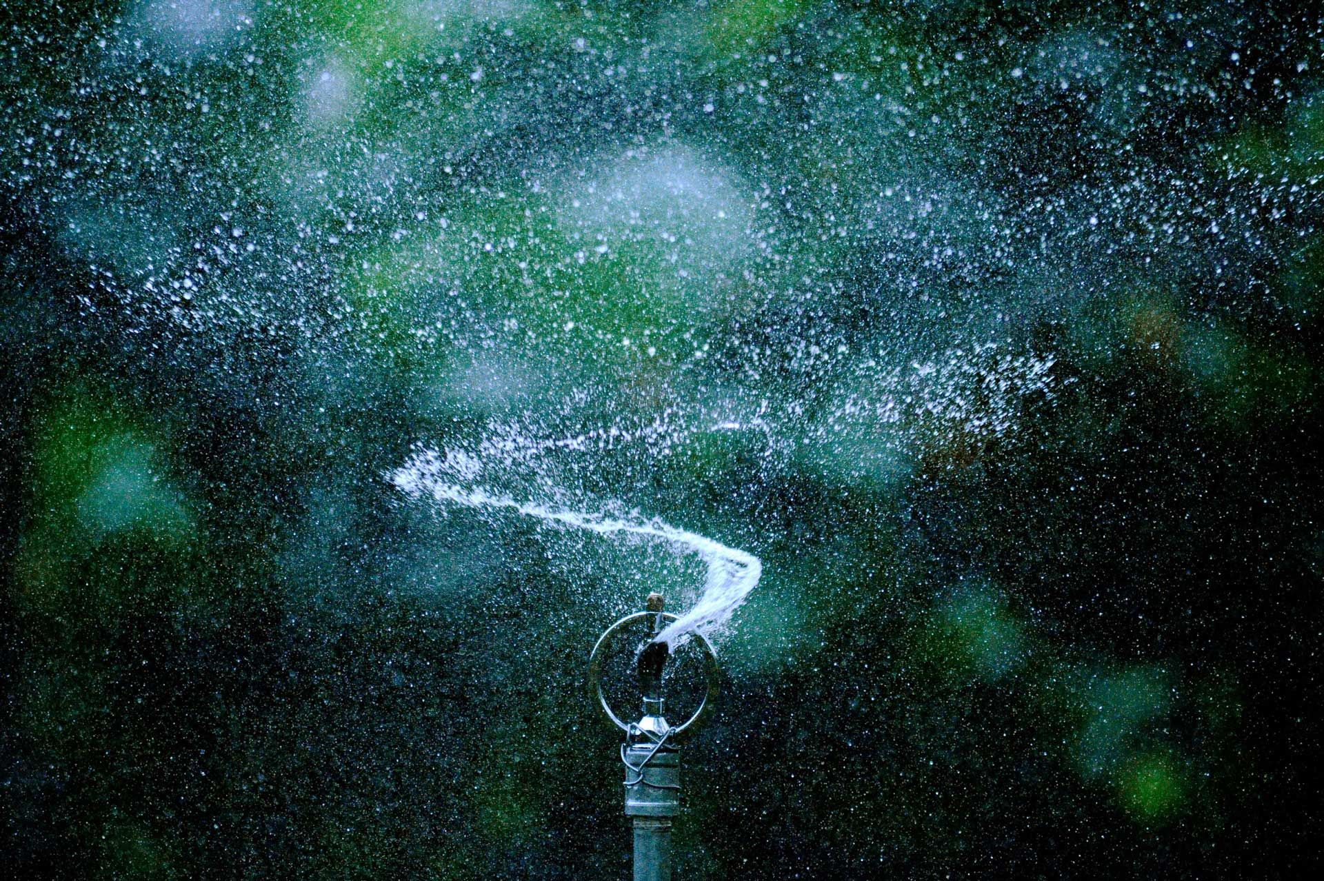 Sprinkler spraying water into the air against a blurry green background.