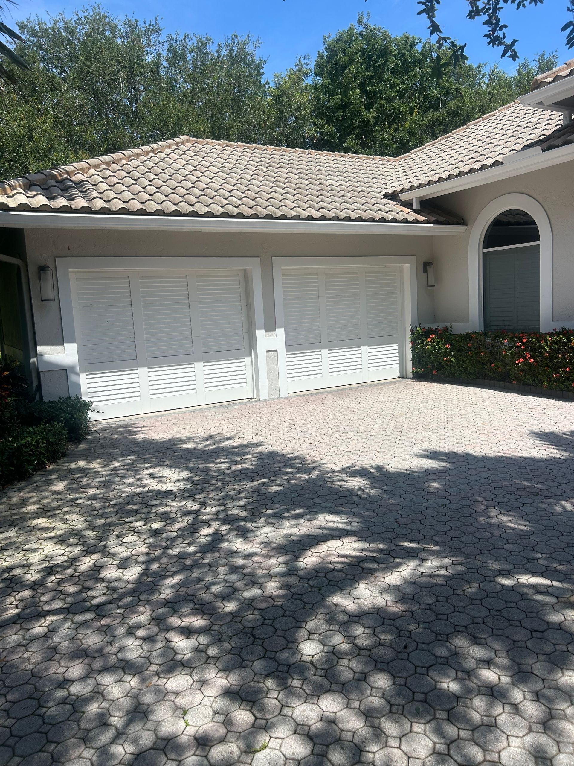 White two-car garage with tiled roof and arched entry, partly shaded by trees on a sunny day
