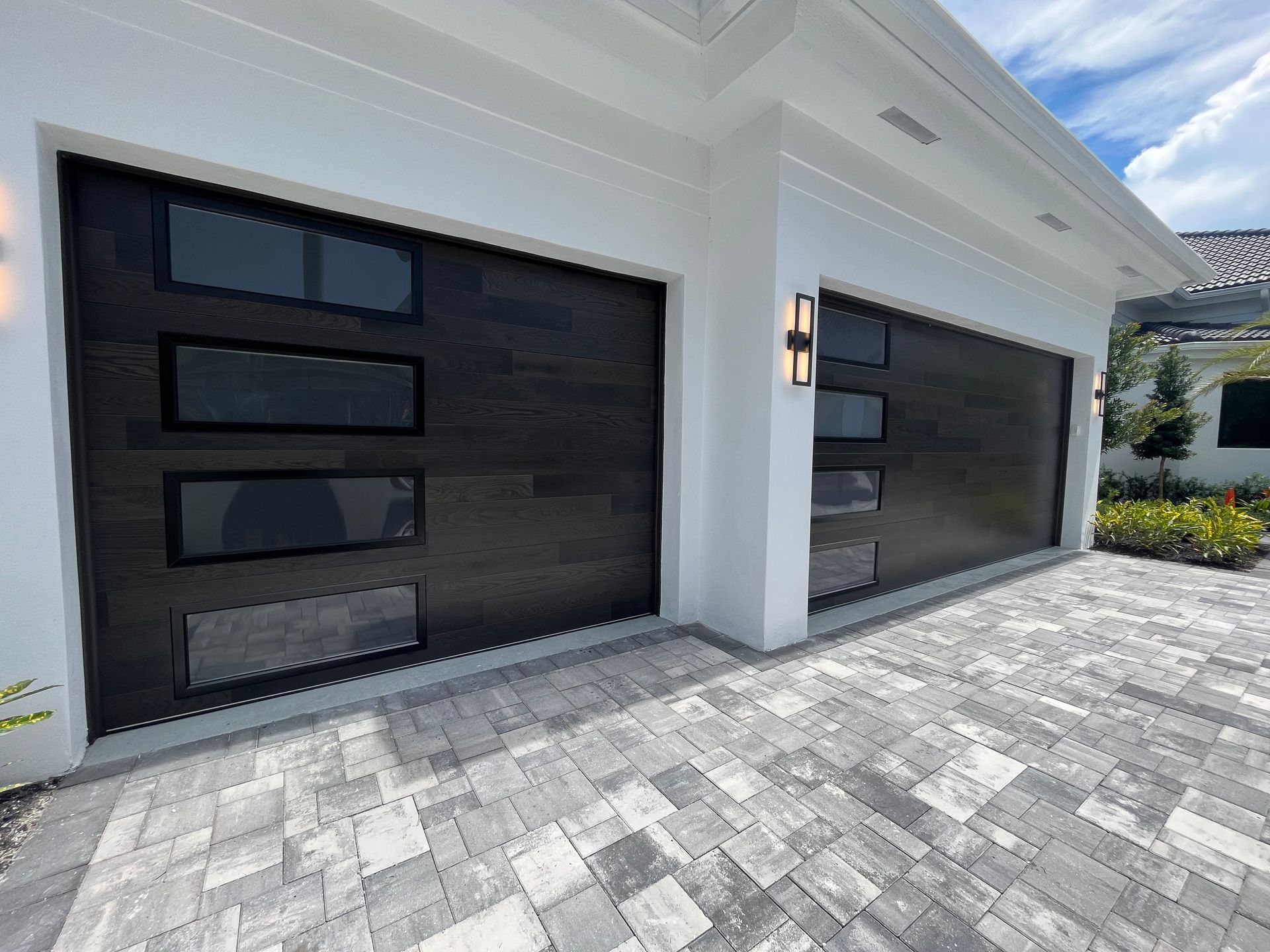 Modern white house exterior with two black garage doors and a gray paved driveway