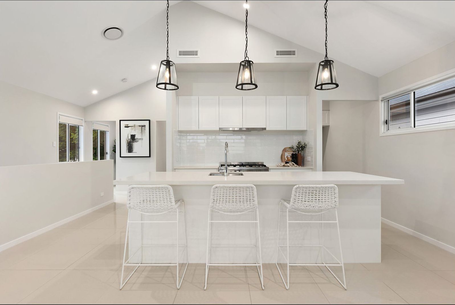 A bright white kitchen with an island and bar stools, under pendant lights.