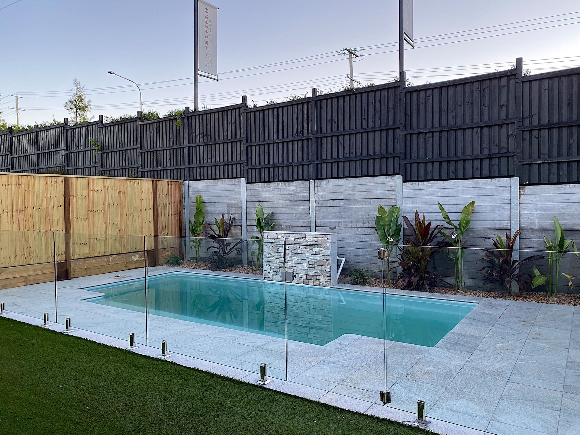 Pool area with clear glass fence, surrounded by wooden and dark gray walls.