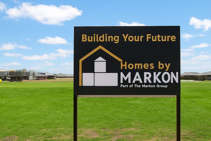 Sign for The Markon Group in front of new homes, set in grassy field under blue sky.