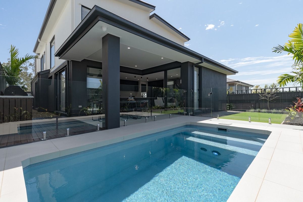 Swimming pool area with a glass fence, surrounded by wooden fences and green turf.