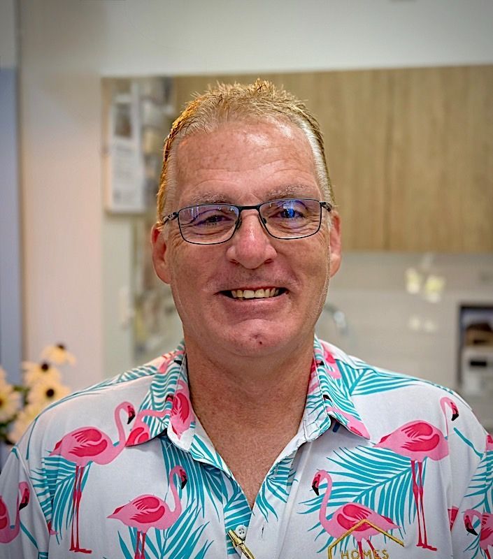 Man with glasses and flamingo shirt smiles in an interior setting.