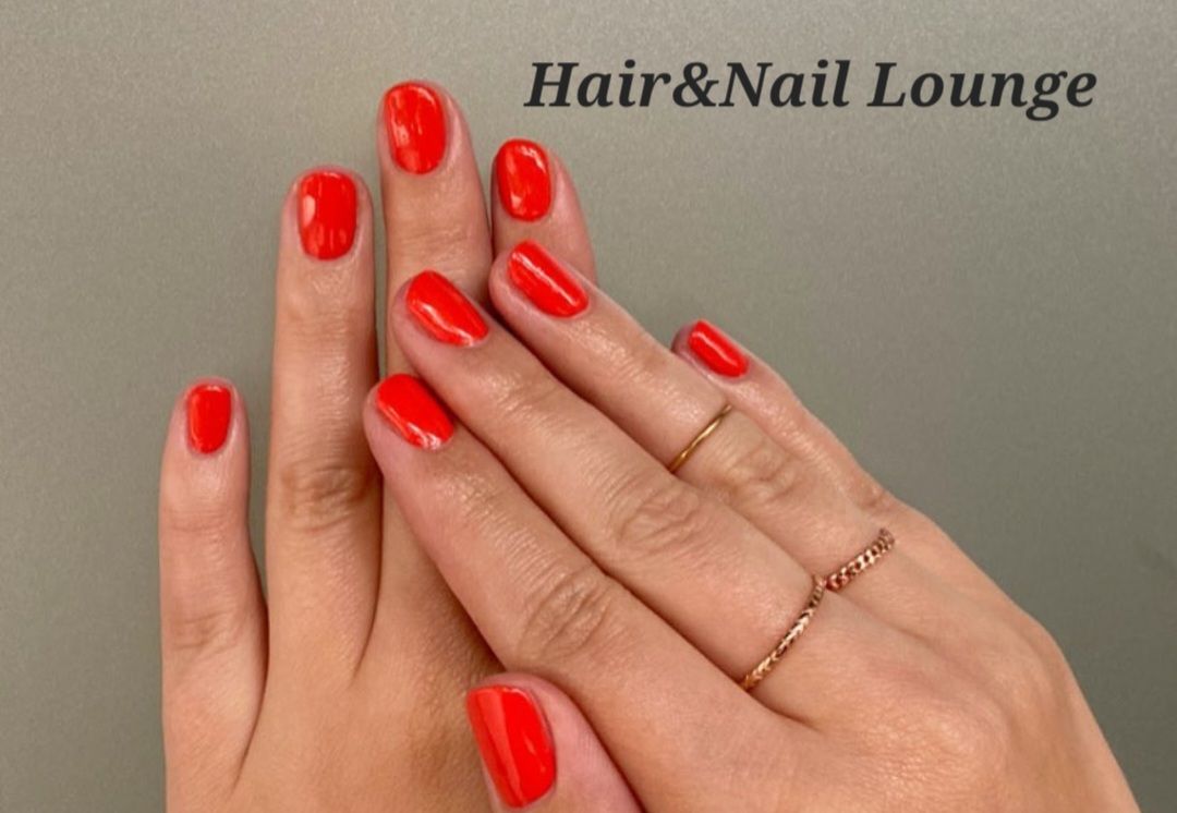 Hände mit leuchtend roter Maniküre und goldenem Ring, im Hintergrund der Schriftzug „Hair&Nail Lounge“.