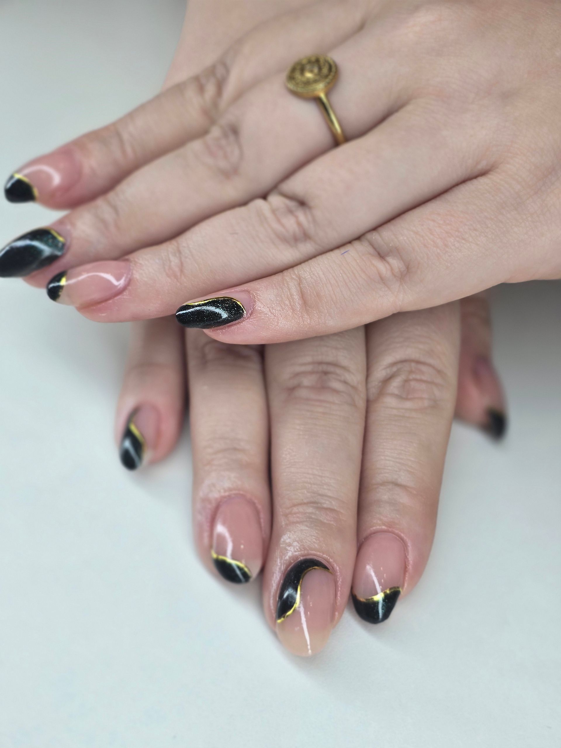 Hände mit schwarz und nudefarben lackierten French-Tip-Nägeln und einem übereinander gestapelten goldenen Ring.