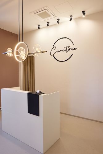Minimalistischer weißer Empfangstresen in einer modernen Lobby mit einem runden Logo an der Wand und Deckenleuchten.