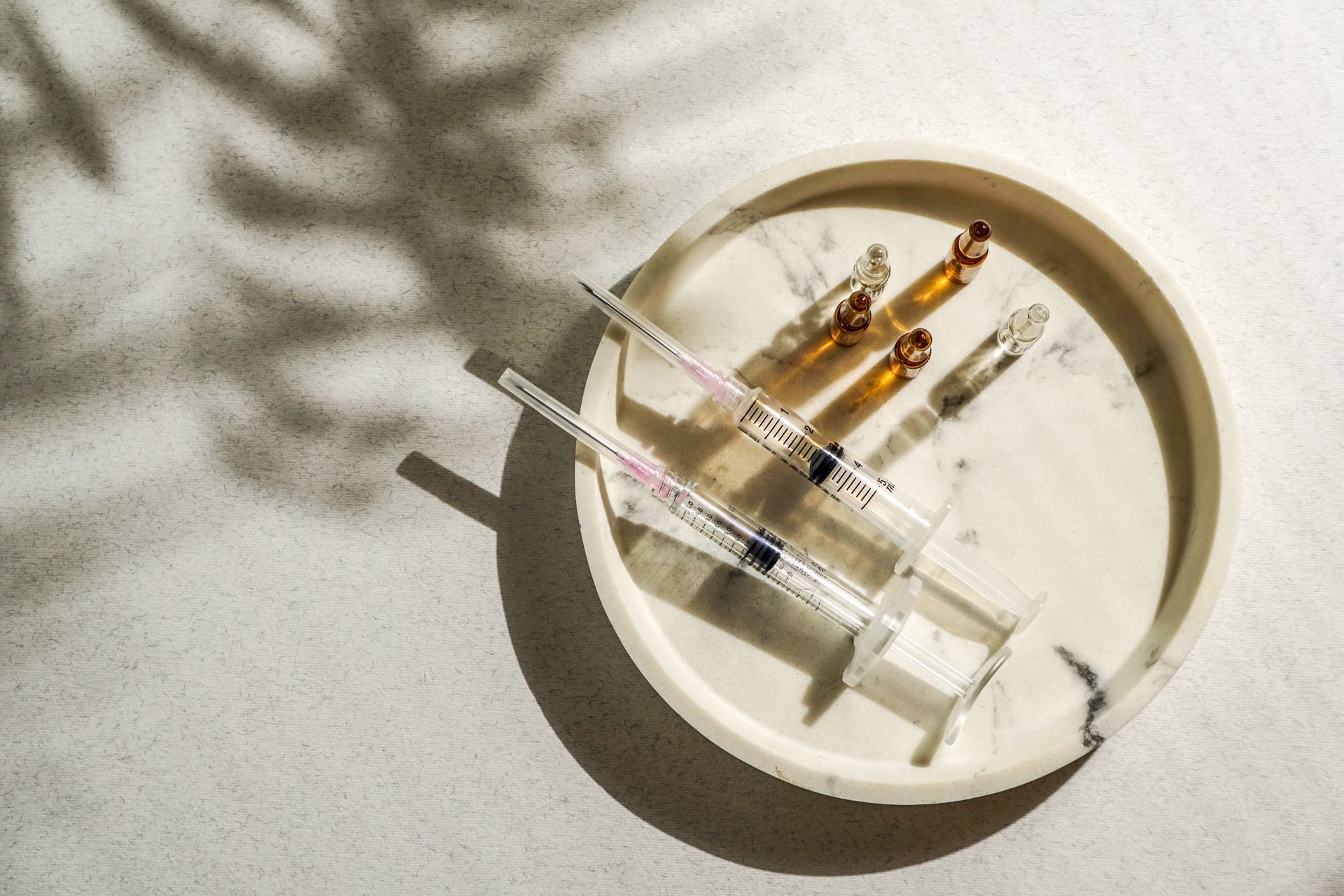 Drei Spritzen und zwei Ampullen in einer weißen Schale auf einer sonnenbeschienenen Oberfläche