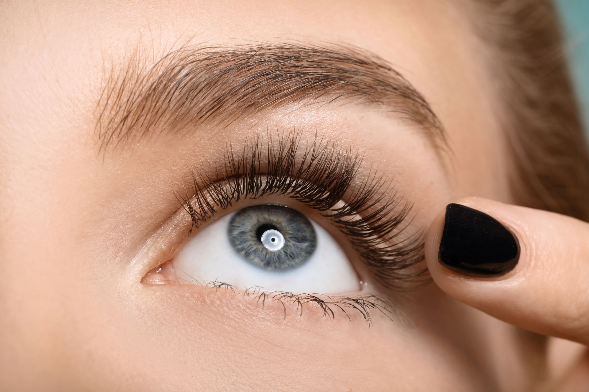 Nahaufnahme eines blauen Auges mit Mascara und einem Finger, der das Unterlid nach unten zieht.