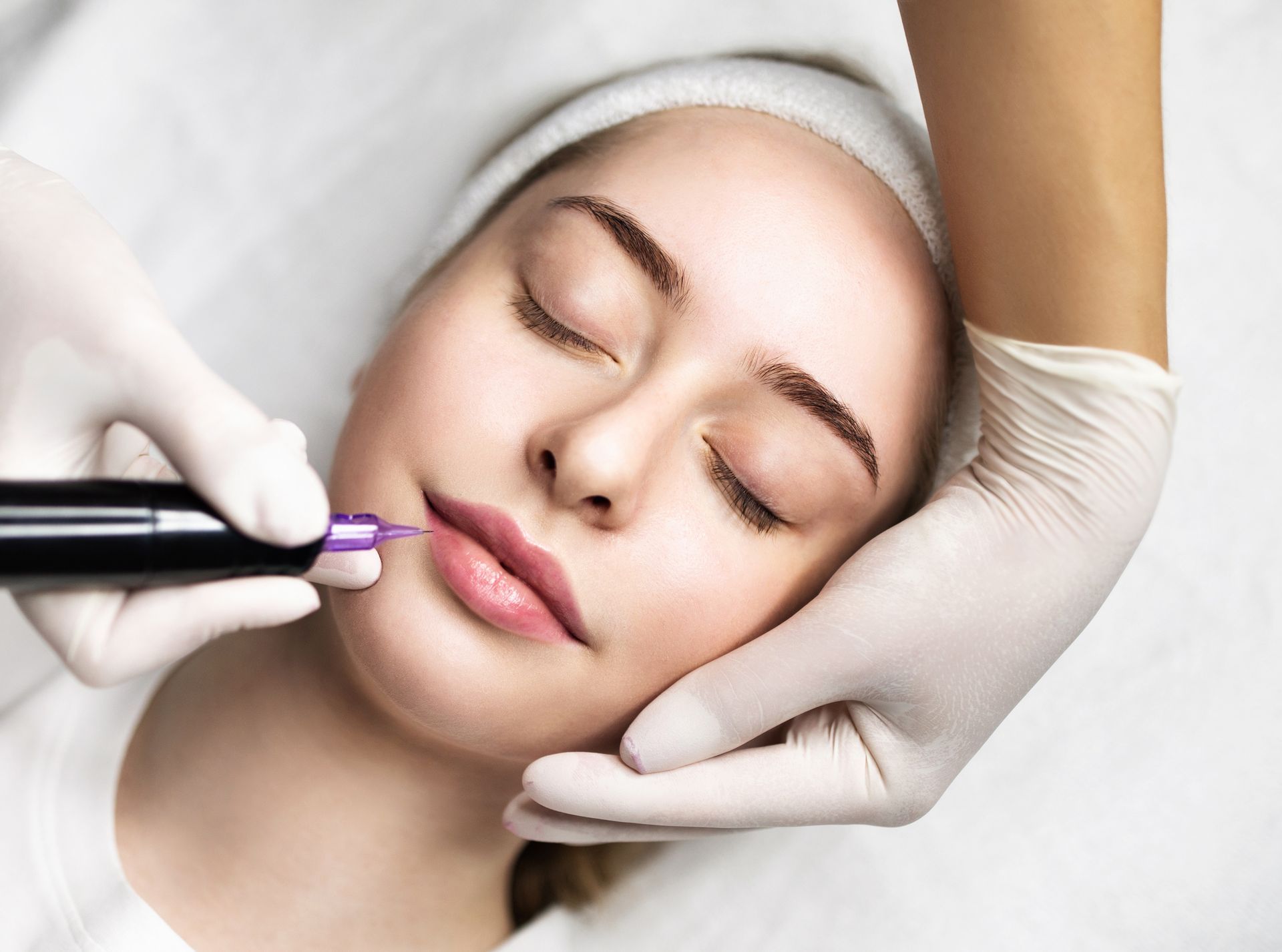 Kosmetische Behandlung der Lippen einer Frau mit behandschuhten Händen unter Anwendung eines violetten Geräts