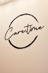 Das „Care.time“-Logo in schwarzer Schrift innerhalb eines kreisförmigen Pinselstrichs auf beiger Wand