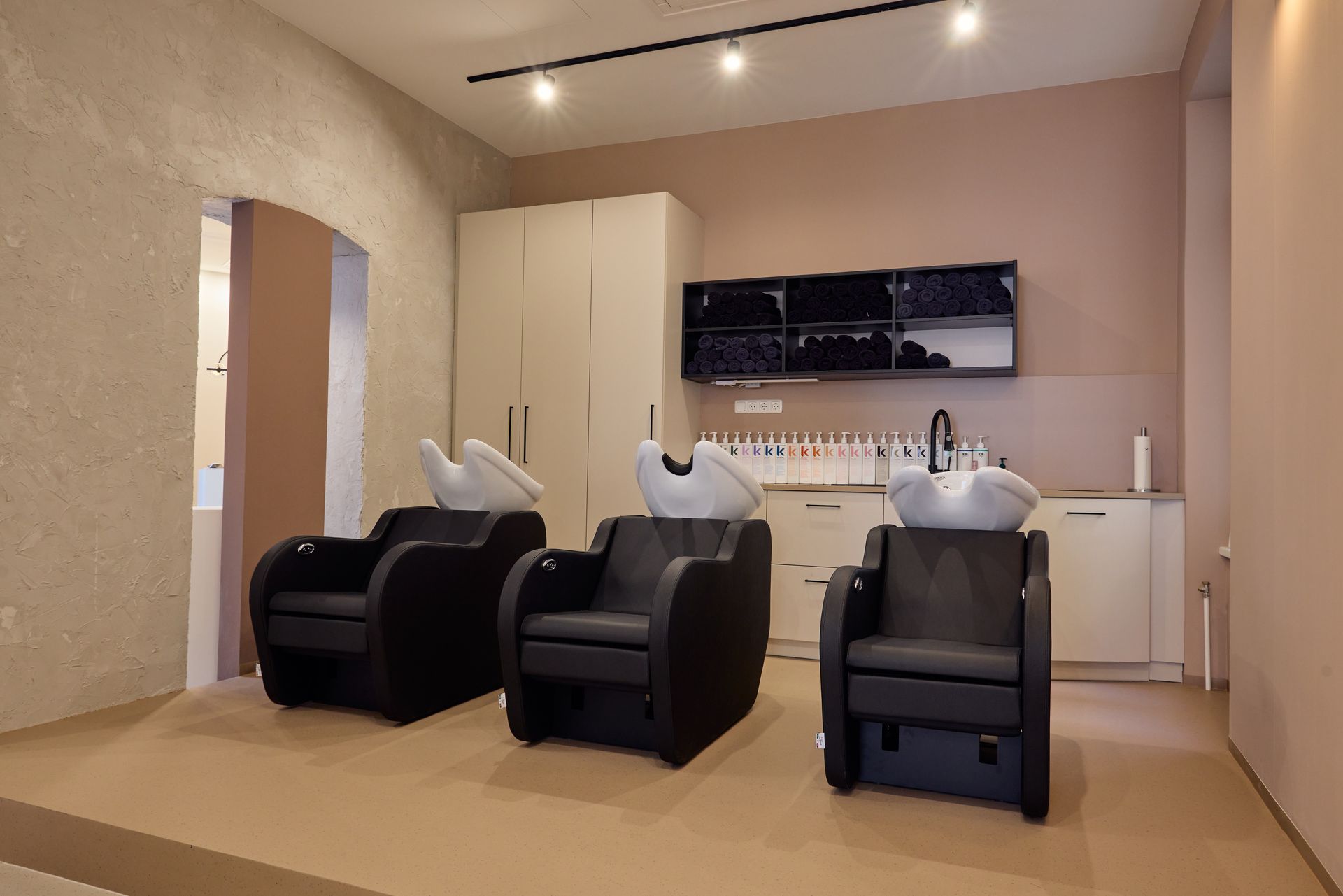 Moderner Friseursalon mit drei schwarzen Waschstühlen, weißen Waschbecken und beigen Wänden
