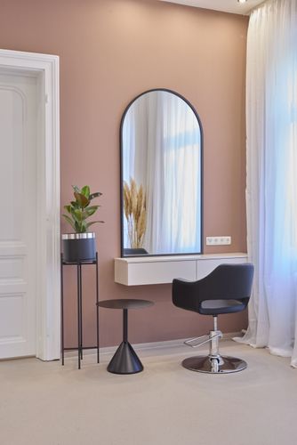 Schminktisch-Setup mit gewölbtem Spiegel, schwarzem Stuhl, kleinem Hocker