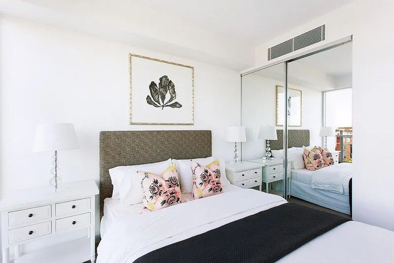 Bright bedroom with a patterned headboard, white bedding, mirrored closet, and framed wall art