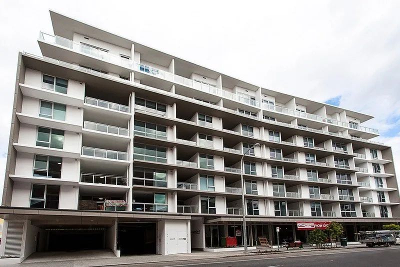 Modern multi-story apartment building with balconies and ground-floor parking area