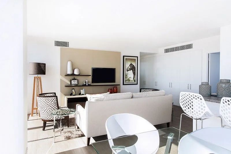 Bright modern living room with white sofas, patterned chairs, a TV, and minimalist decor