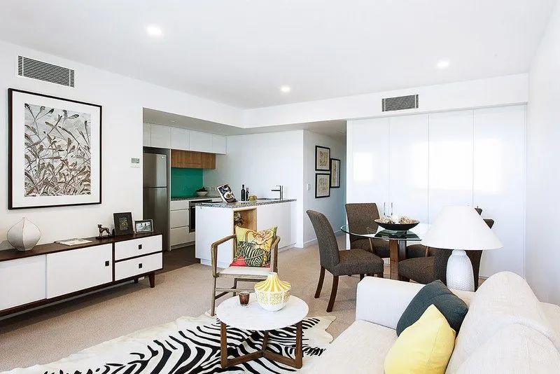 Bright open-plan living room with white sofa, dining table, kitchen, and large windows