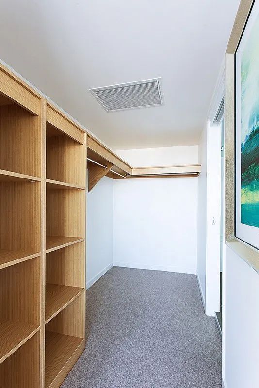 Empty narrow hallway with wooden shelving on the left, white walls, gray carpet, and a framed picture on the right.