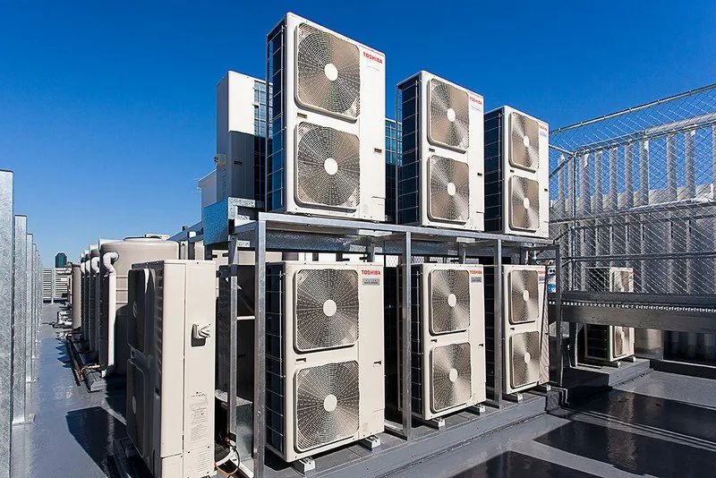 Rows of rooftop HVAC units and cooling fans on a metal platform under a clear blue sky