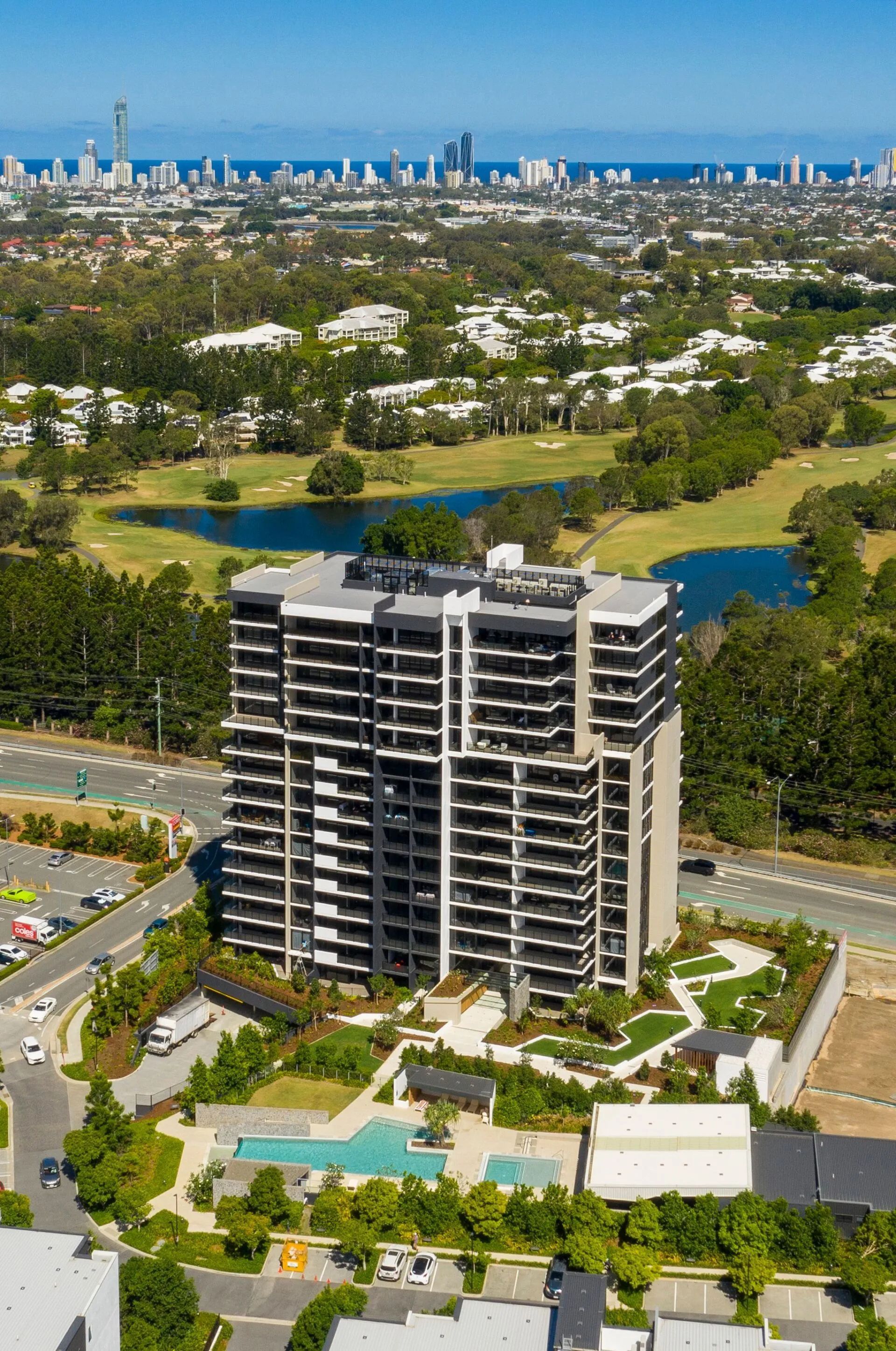 High-rise apartment tower beside a pool and green park, with city skyline in the distance