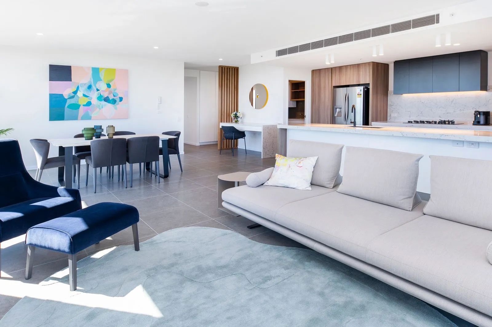 Modern open-concept living room with white sofa, blue chair, dining area, and kitchen island with wood accents