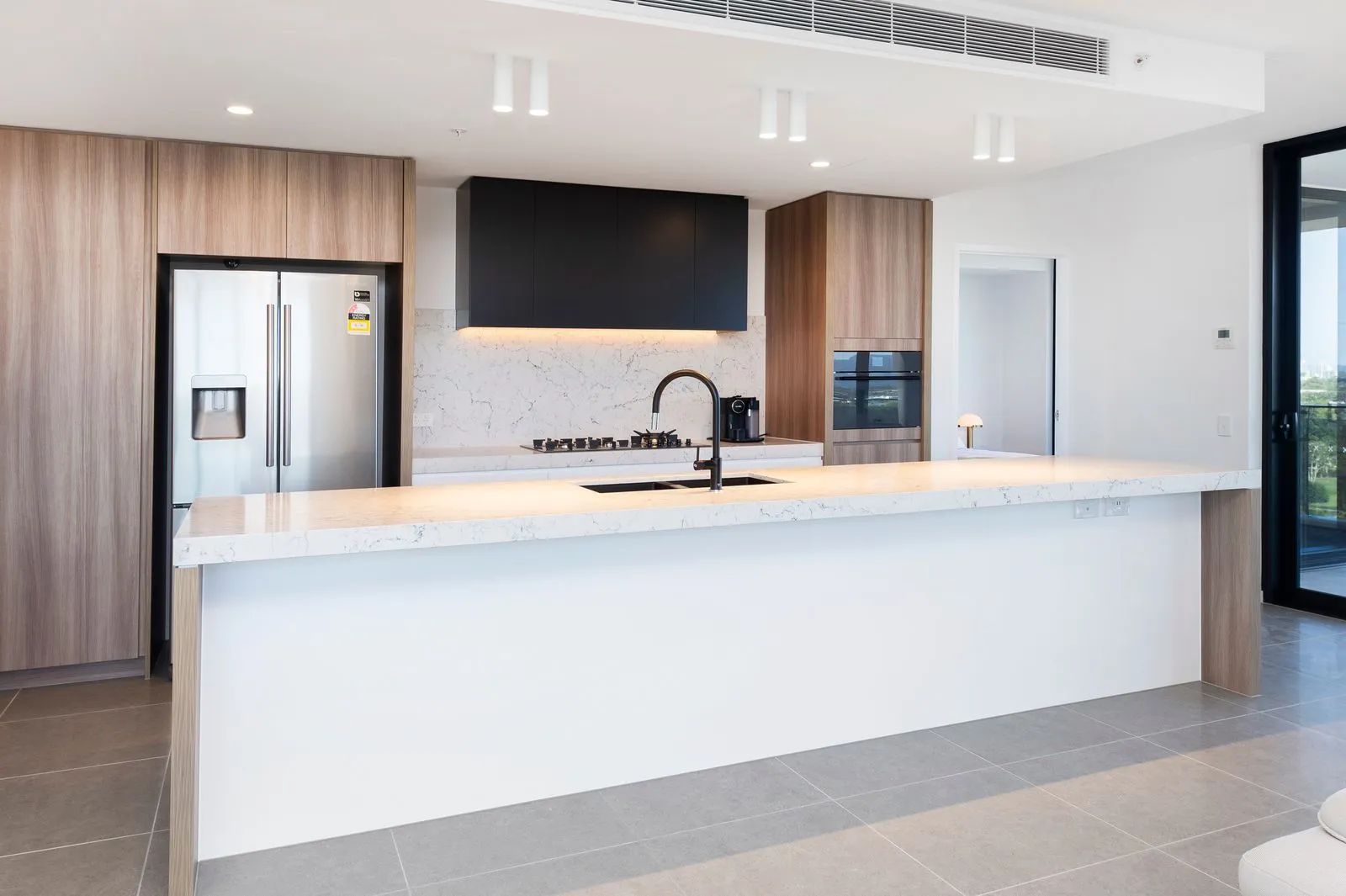 Modern kitchen with white island, stainless steel appliances, wood cabinets, and black fixtures