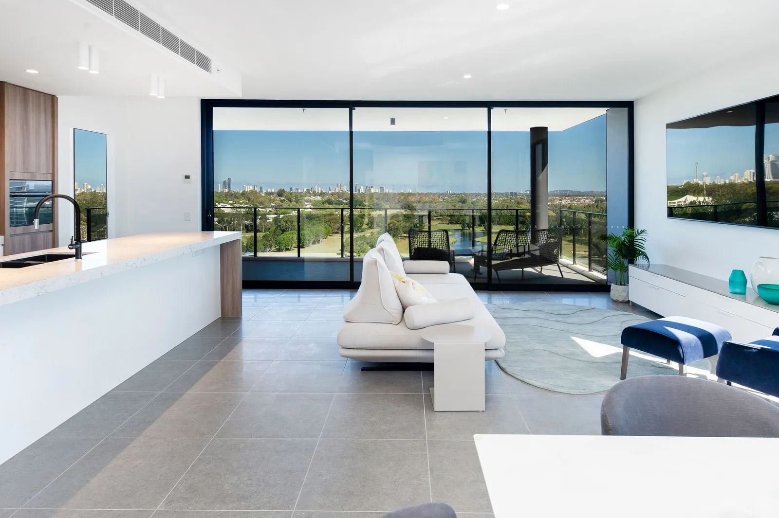 Modern living room with white sofas, large glass windows, and a city view