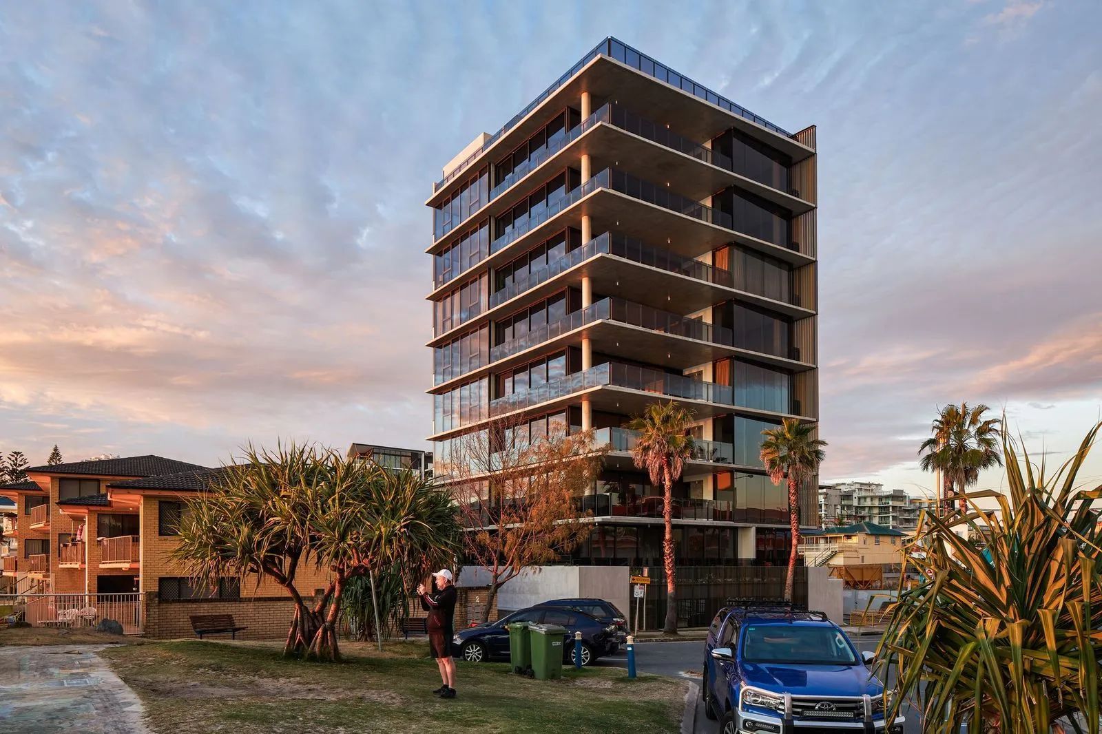 Modern high-rise building under construction at sunset, with cars and trees in the foreground