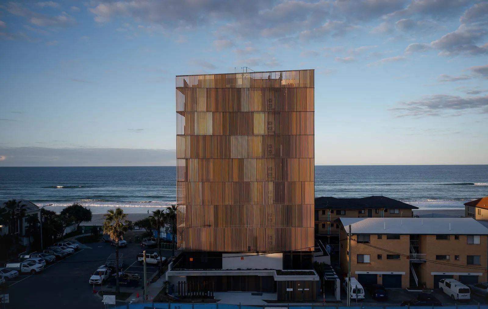 Gold-toned high-rise tower by the ocean at sunset, with a cloudy sky and nearby buildings