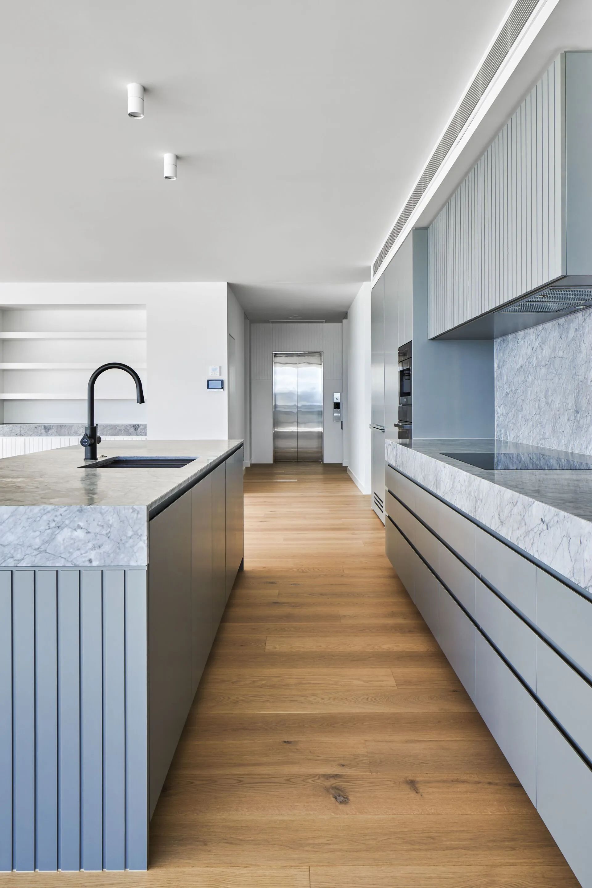 Modern kitchen with gray island, black faucet, wood floor, and large windows.