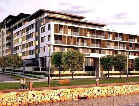 Modern multi-story apartment building with balconies beside a waterfront promenade at sunset