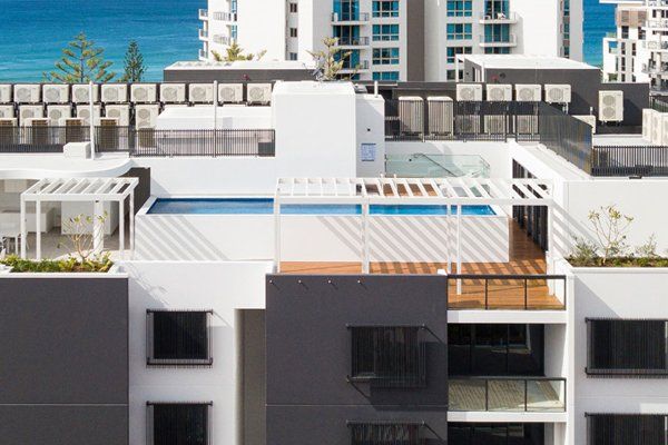 Modern white rooftop terrace with pergola, lounge seating, and sea-view city buildings in the background