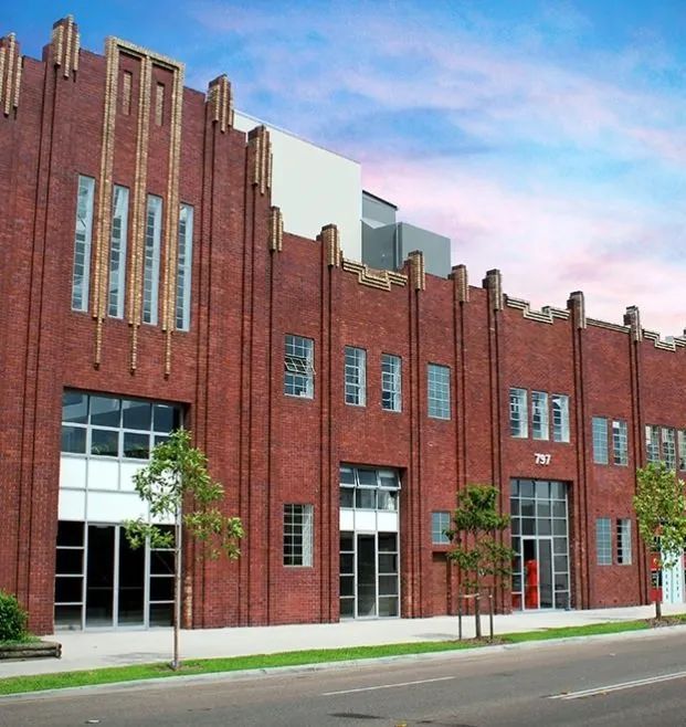 Red brick Art Deco-style building with tall windows along a quiet street at dusk