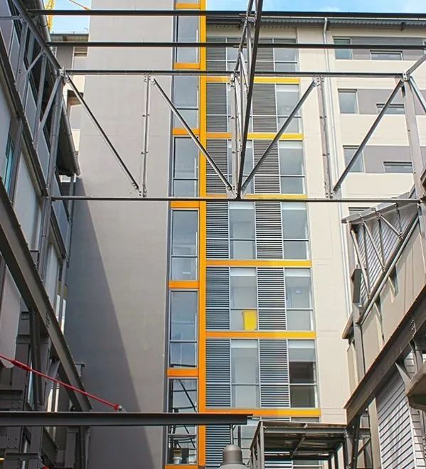 Modern building courtyard with a tall yellow-framed glass facade between gray walls