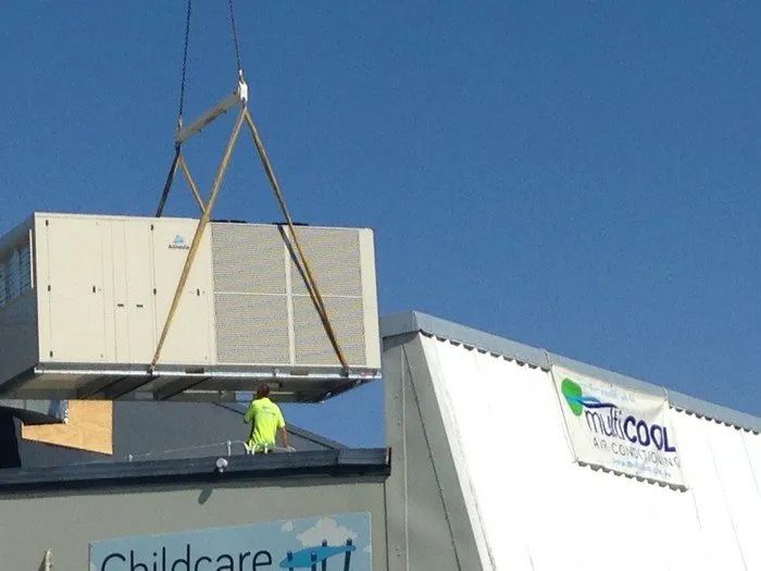 Crane lifting a large white container onto a rooftop beside a childcare center sign.