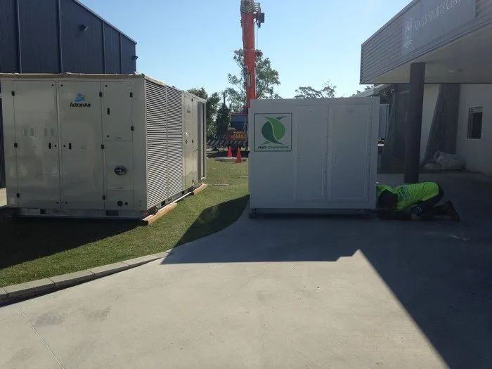 Outdoor utility area with large white equipment units and a worker in a neon vest beside a building
