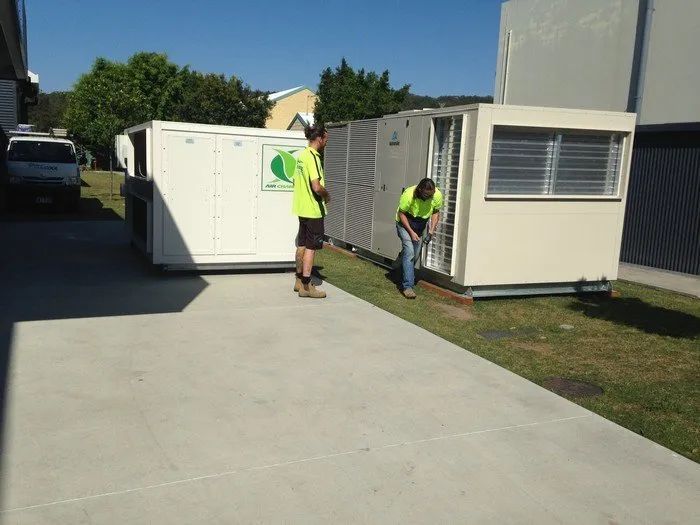 Workers moving white portable offices beside a building on a sunny driveway