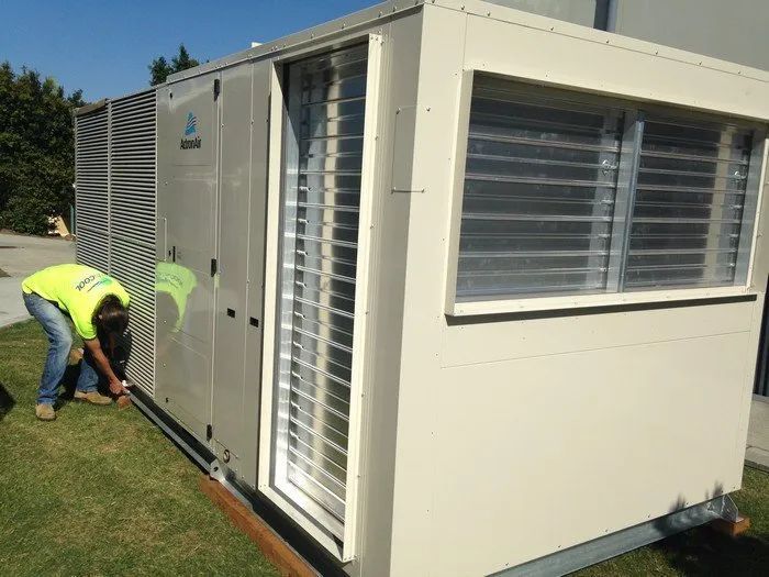 Worker in neon vest installing a cream-colored portable building outdoors