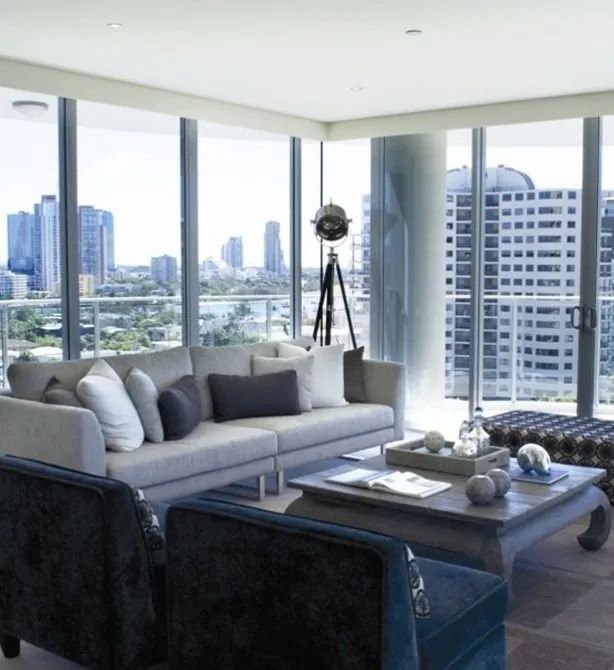 Modern living room with gray sofas, coffee table, and floor-to-ceiling windows overlooking a city skyline