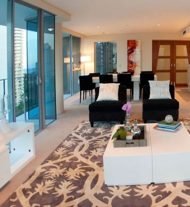Modern living room with floor-to-ceiling windows, black chairs, and a patterned rug near a balcony view