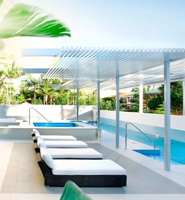 Modern poolside lounge with white sunbeds and blue water under a shaded pergola