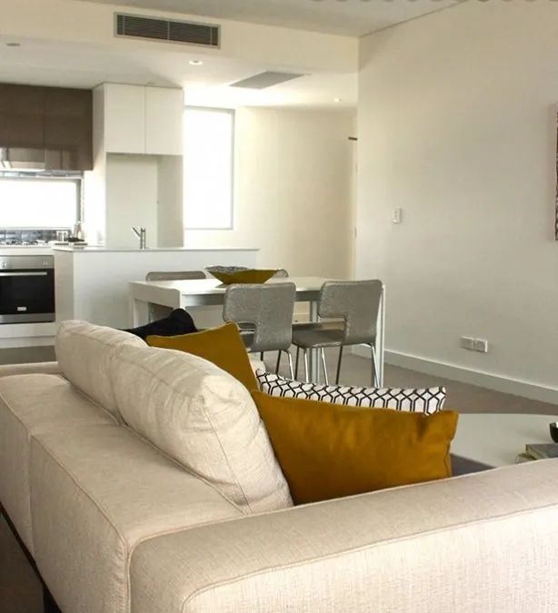 Bright open-plan living room with cream sofa, mustard pillows, dining table, and kitchen in the background