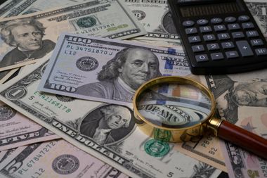 U.S. dollar bills with a magnifying glass and calculator, suggesting financial analysis