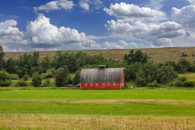 Red barn in a green field beneath a cloudy blue sky