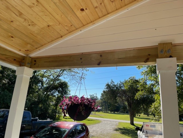 View from under a porch roof, showing the ceiling, support beams, and a hanging basket of flowers. View from under a porch roof, showing the ceiling, support beams, and a hanging basket of flowers.