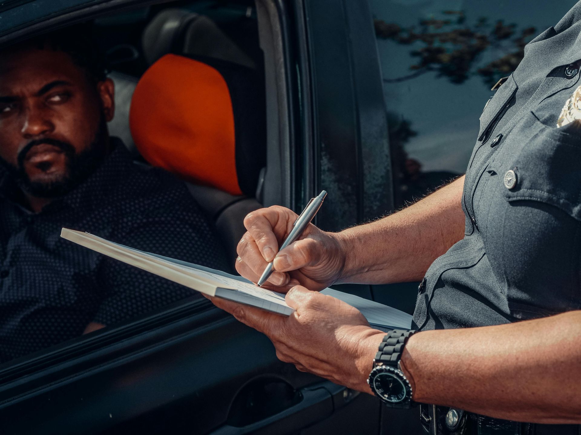 Officer writing in a notebook beside a car window while speaking to the driver inside